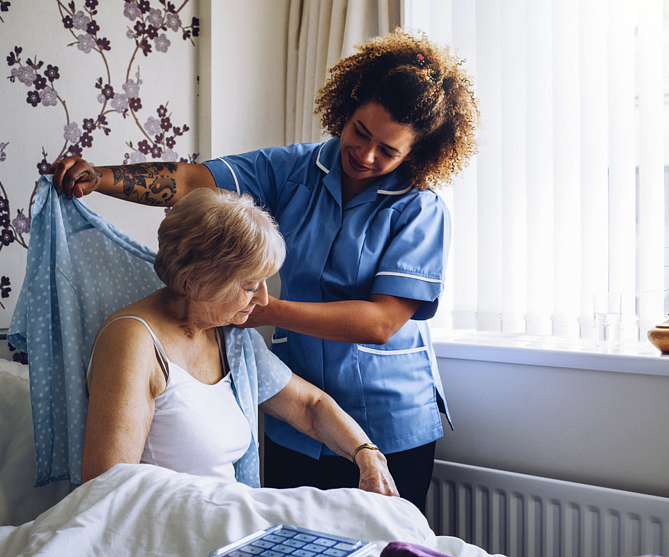 caregiver helping the senior woman to wear her clothes